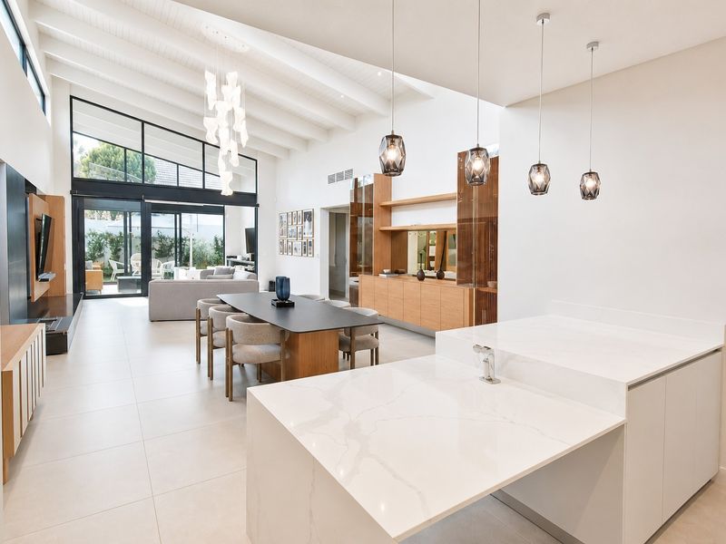 Spacious open-plan living area featuring a modern kitchen island, vaulted ceilings with exposed beams, and seamless flow to the outdoor patio through large glass doors.