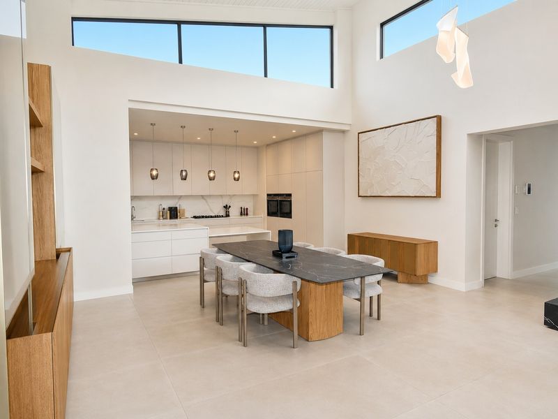 Modern open-plan living and kitchen area featuring high ceilings, clerestory windows, sleek cabinetry, integrated appliances, and premium tiled flooring with a feature fireplace.