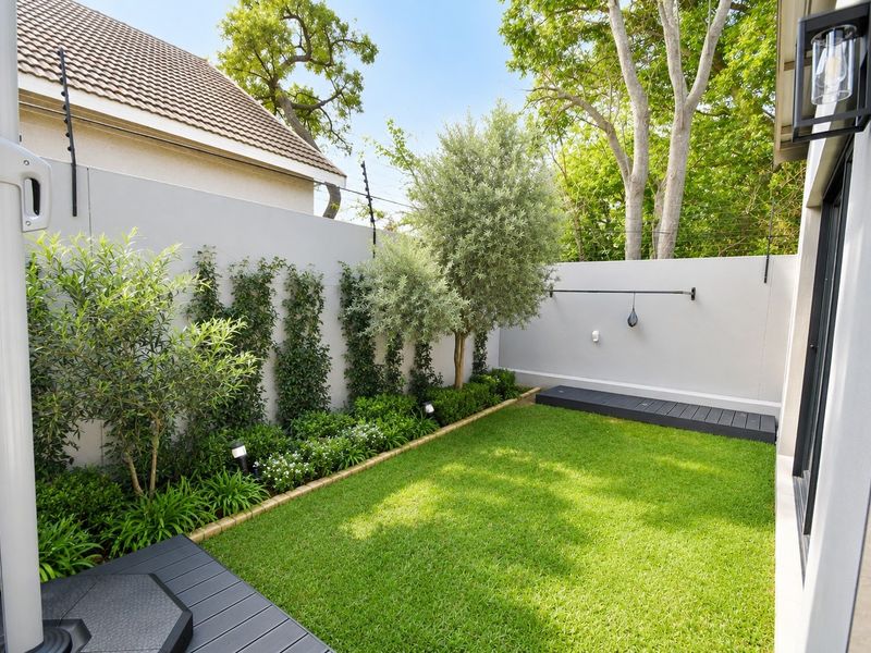 A well-maintained private garden featuring a manicured lawn, landscaped borders, boundary walls with electric fencing, and modern timber decking.