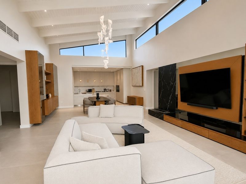 Spacious open-plan living area featuring vaulted ceilings with exposed beams, clerestory windows, custom built-in cabinetry, and a striking marble fireplace feature wall.