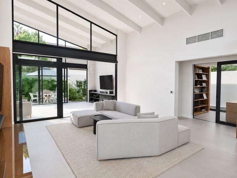 Spacious modern living room featuring high vaulted ceilings with exposed beams, large format floor tiles, and expansive black-framed sliding doors opening to the patio.