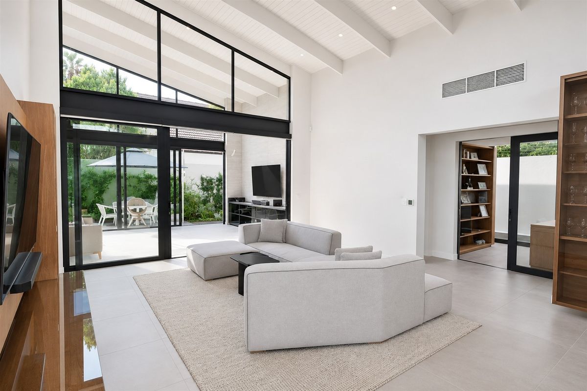 Spacious modern living room featuring high vaulted ceilings with exposed beams, large format floor tiles, and expansive black-framed sliding doors opening to the patio.