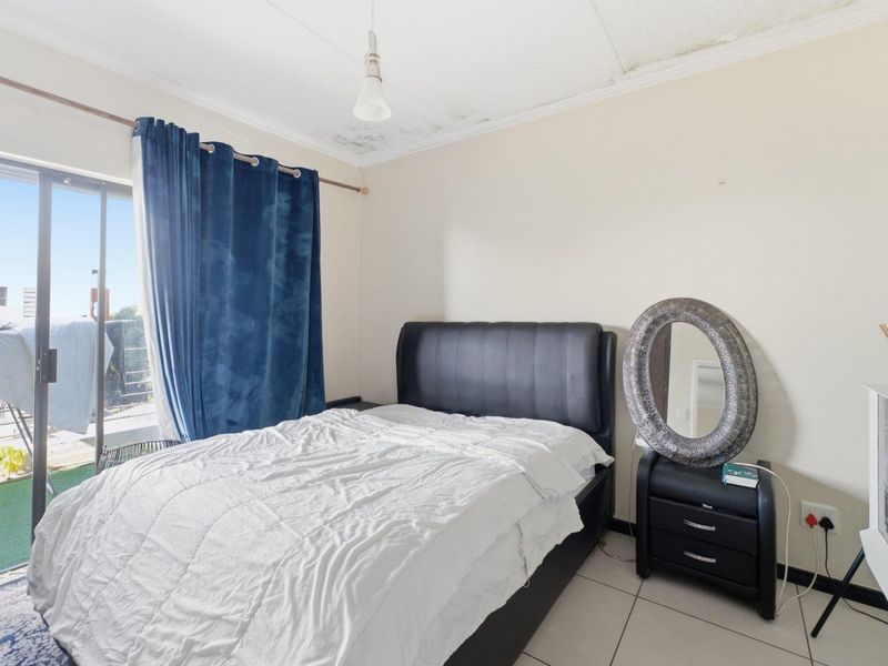 Bedroom featuring tiled flooring and a sliding glass door leading to a balcony, with visible water damage requiring ceiling repairs.