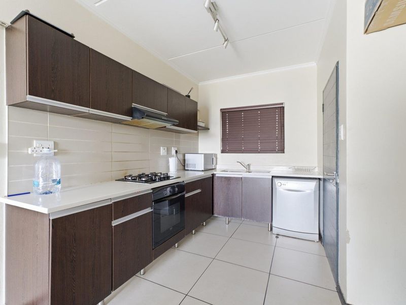 A functional kitchen featuring dark wood cabinetry, a gas hob, electric oven, extractor fan, and tiled flooring with a neutral backsplash.