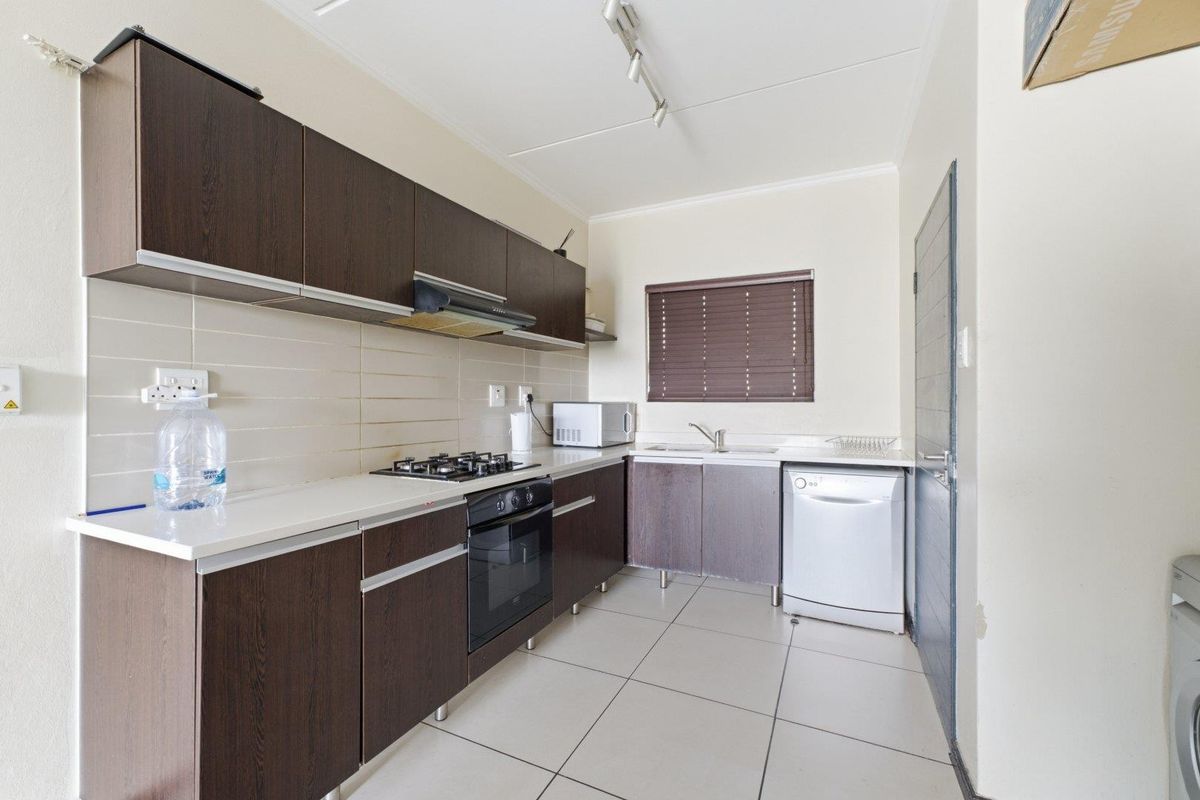 A functional kitchen featuring dark wood cabinetry, a gas hob, electric oven, extractor fan, and tiled flooring with a neutral backsplash.