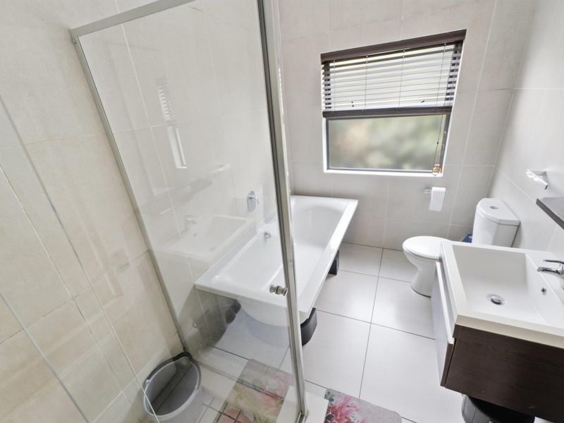 A clean, modern bathroom featuring a glass-enclosed shower, a bathtub, a vanity basin, and a toilet, finished with neutral wall and floor tiles.