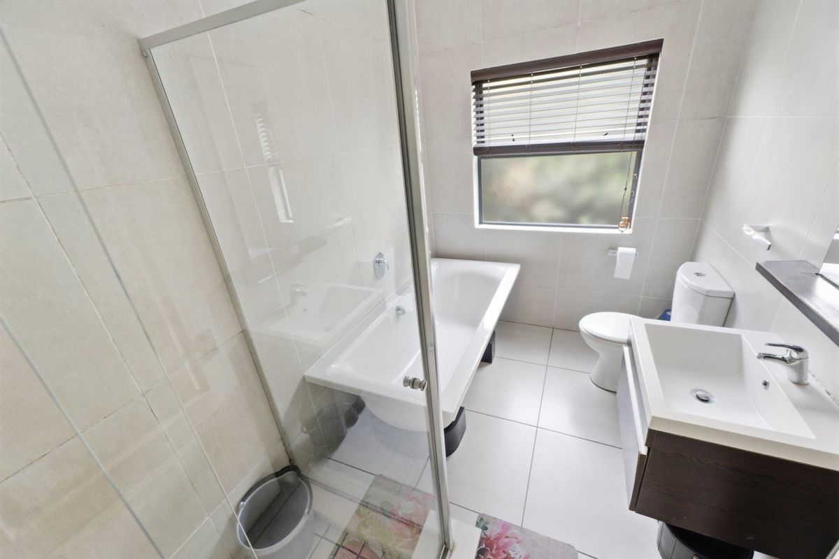 A clean, modern bathroom featuring a glass-enclosed shower, a bathtub, a vanity basin, and a toilet, finished with neutral wall and floor tiles.