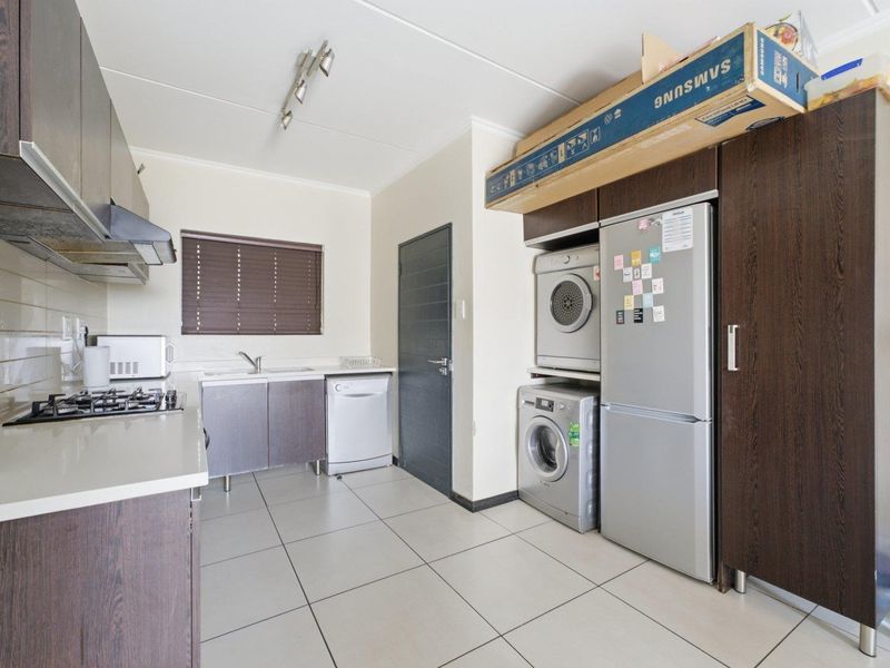 A functional kitchen featuring dark wood cabinetry, a gas hob with extractor, tiled flooring, and dedicated space for laundry appliances.