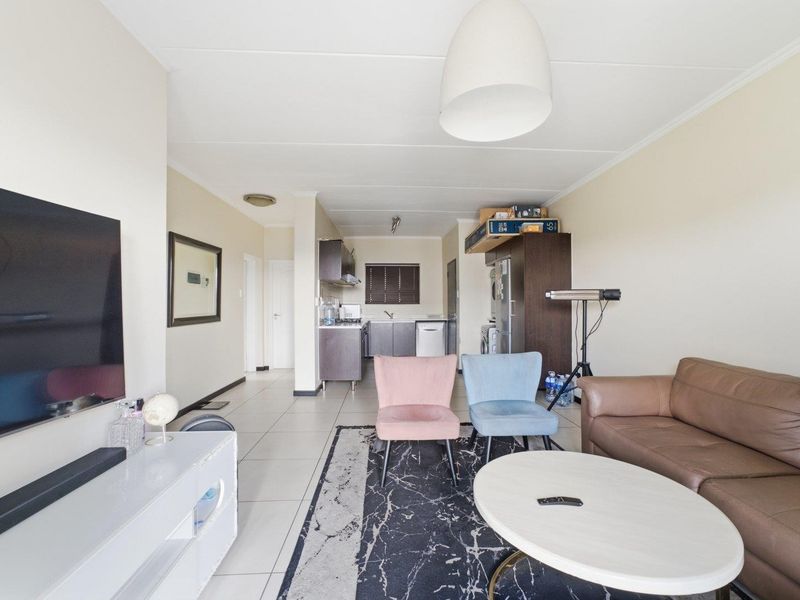 Open-plan living area featuring tiled flooring and a compact kitchen with built-in cabinetry and sink, creating a functional combined living and cooking space.