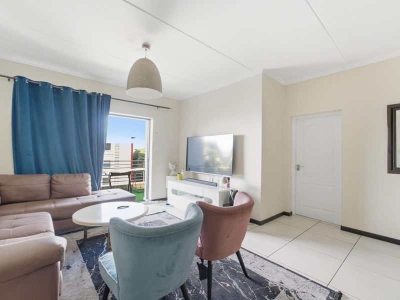 A bright living room featuring tiled flooring, a pendant light, and a sliding glass door providing access to an outdoor balcony area.