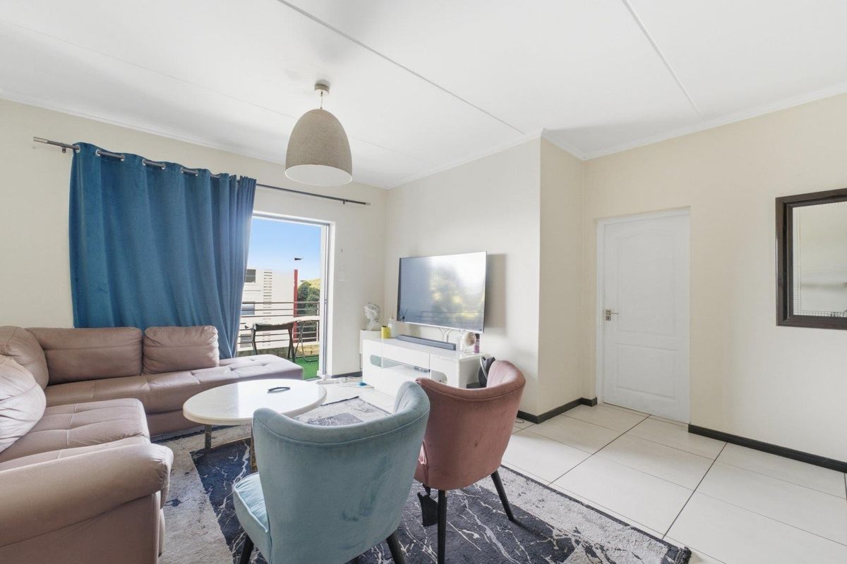 A bright living room featuring tiled flooring, a pendant light, and a sliding glass door providing access to an outdoor balcony area.