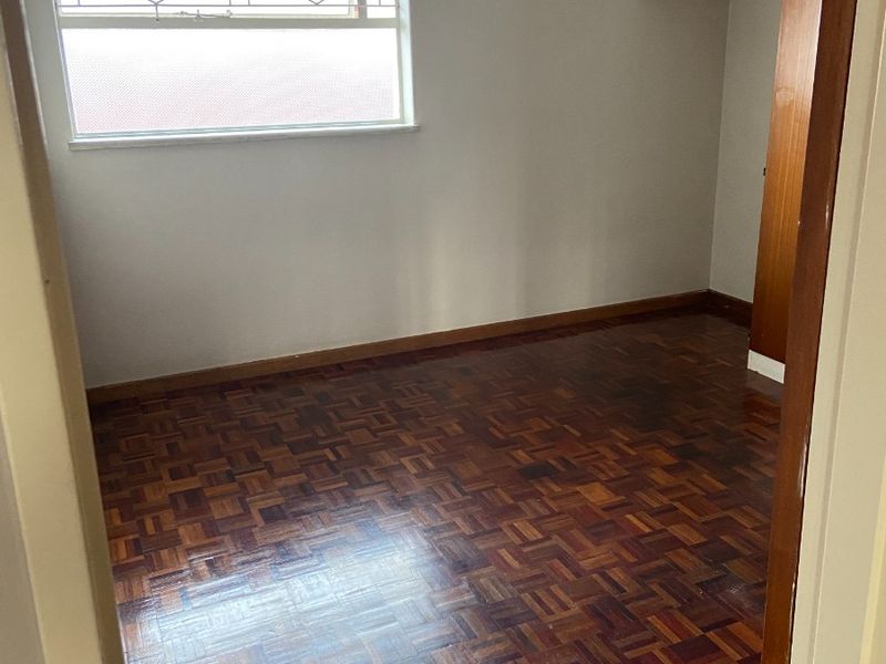 An empty bedroom featuring traditional parquet flooring, built-in wooden cupboards, and a window fitted with security bars.
