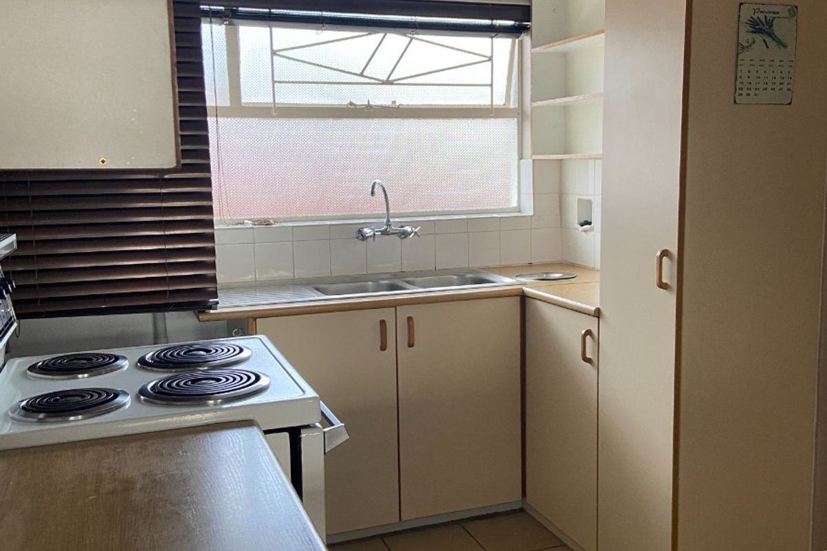 A functional kitchen featuring built-in cabinetry, a double basin sink, and an electric stove, offering a practical layout with potential for modern updates.
