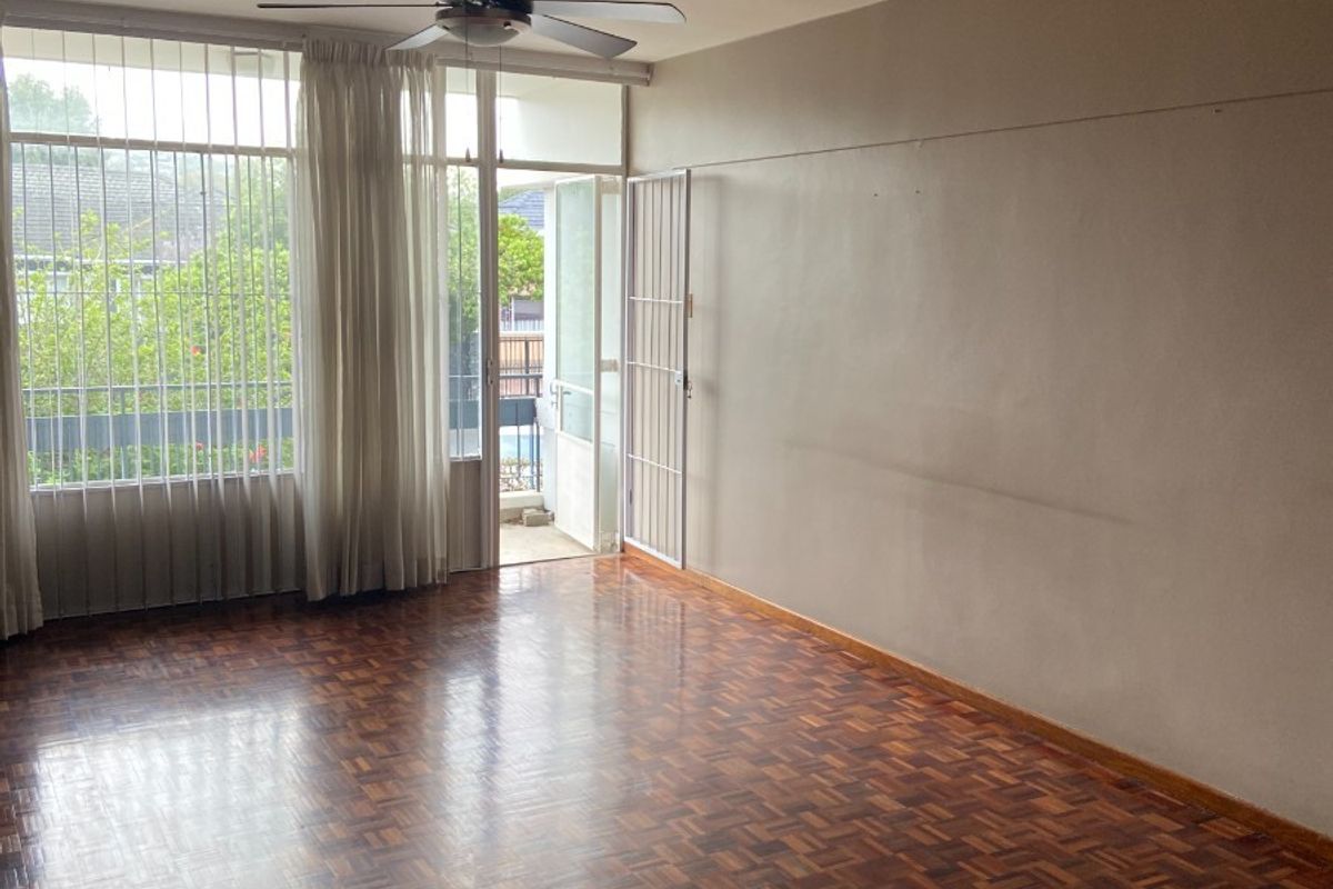 Spacious living area featuring classic parquet flooring, a ceiling fan, and direct access to a balcony through a secure door.