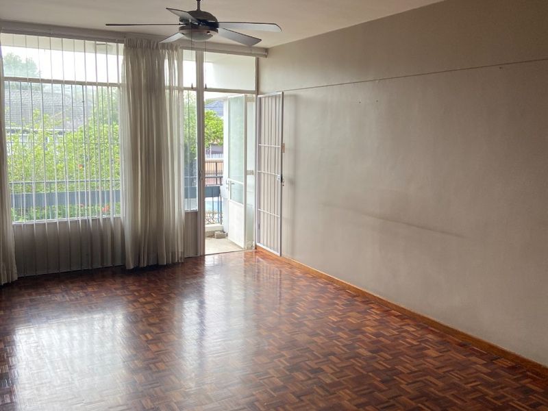 Spacious living area featuring classic parquet flooring, a ceiling fan, and direct access to a balcony through a secure door.