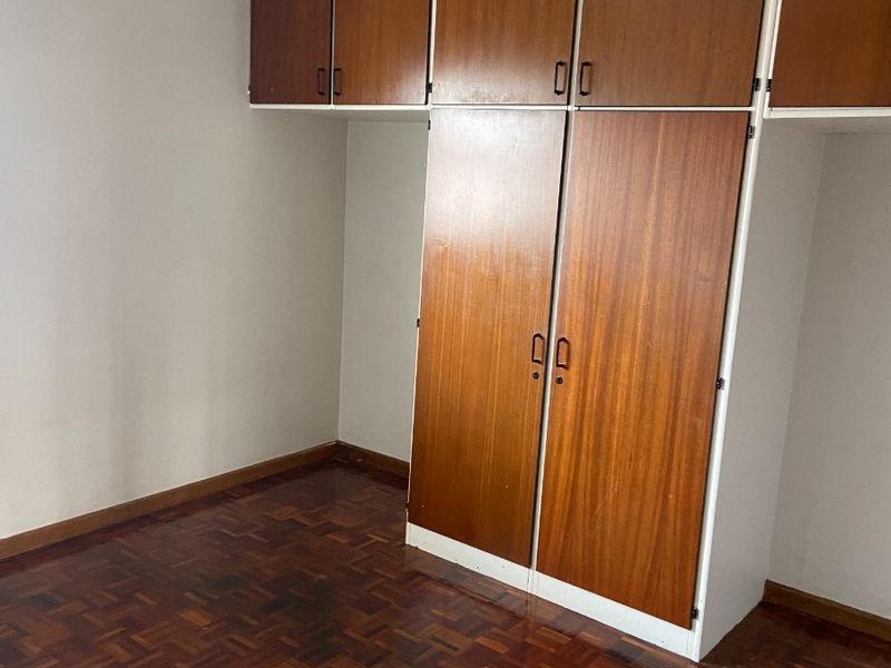 A bedroom featuring original parquet flooring and extensive built-in wooden cabinetry with overhead storage compartments.