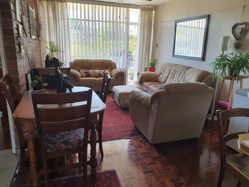 Open-plan living and dining area featuring classic parquet flooring, an exposed brick feature wall, and large sliding doors leading to a balcony.