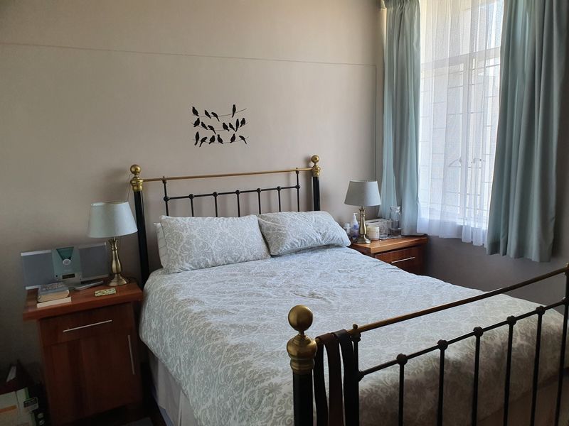 A well-lit bedroom featuring neutral wall tones and a large window with fitted curtain rails, providing a comfortable and functional sleeping space.