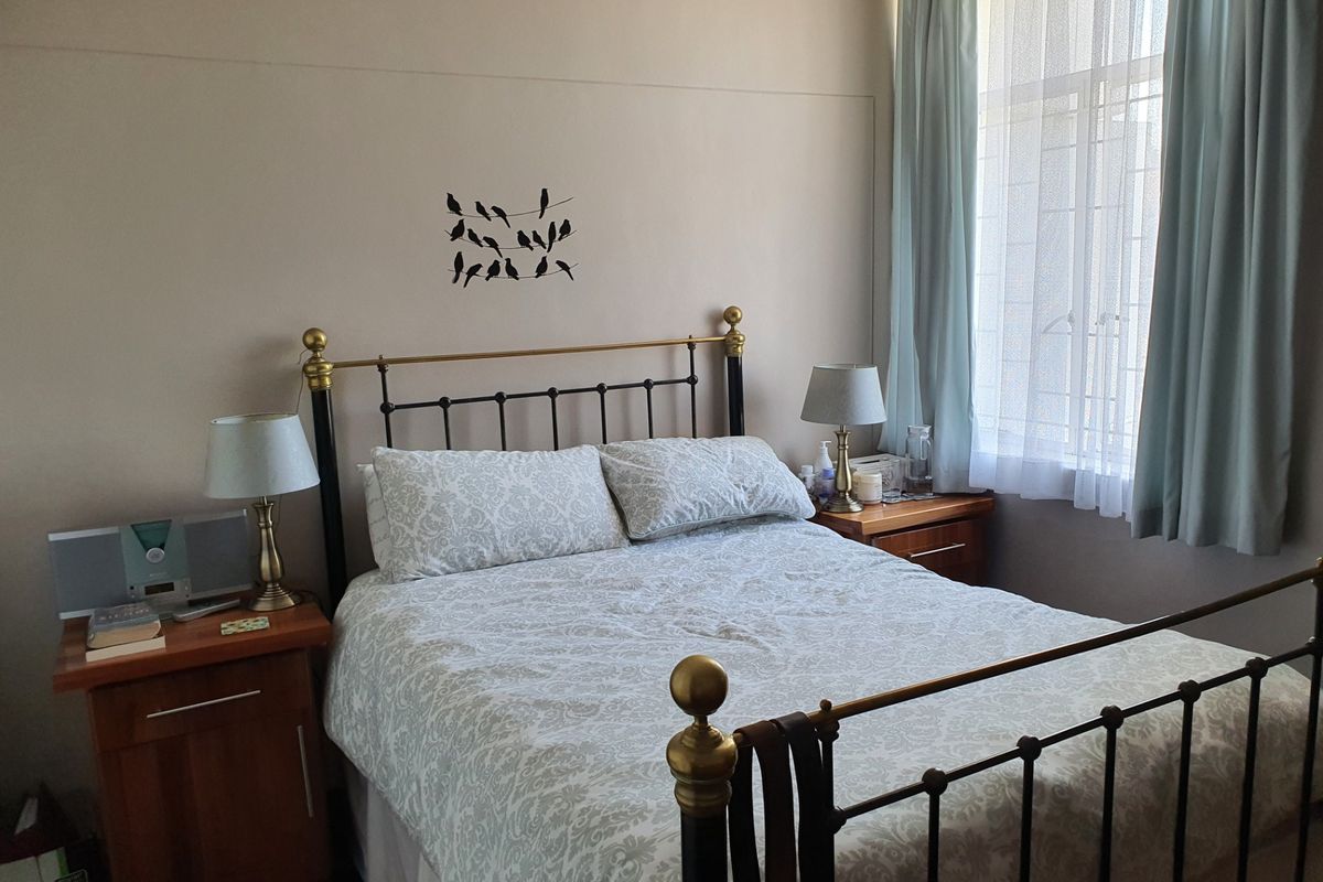 A well-lit bedroom featuring neutral wall tones and a large window with fitted curtain rails, providing a comfortable and functional sleeping space.