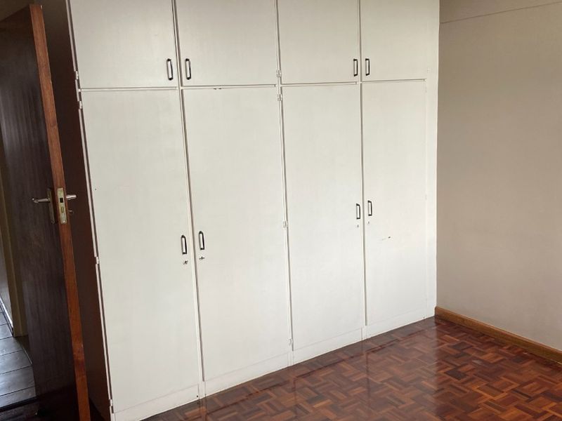 A vacant bedroom featuring classic parquet flooring and extensive floor-to-ceiling built-in cupboards with white cabinetry.