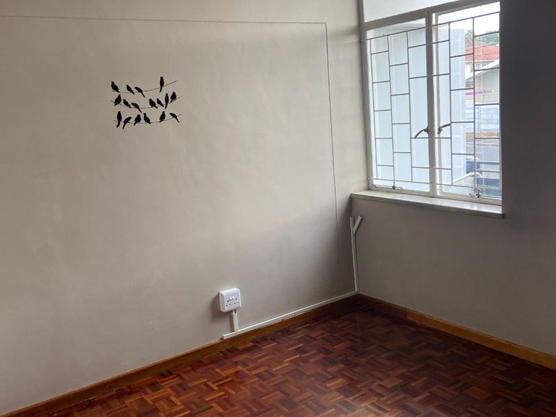 An empty bedroom featuring polished parquet flooring, a large window with security bars, and neutral wall finishes.