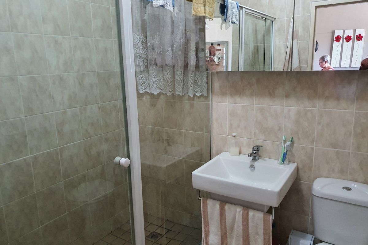 A functional bathroom featuring a shower enclosure, wall-mounted basin, toilet, and a mirrored medicine cabinet with neutral wall tiling.