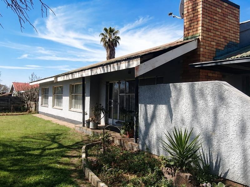 Rear view of the house featuring a brick chimney, corrugated metal roof, and a covered patio area overlooking the garden.