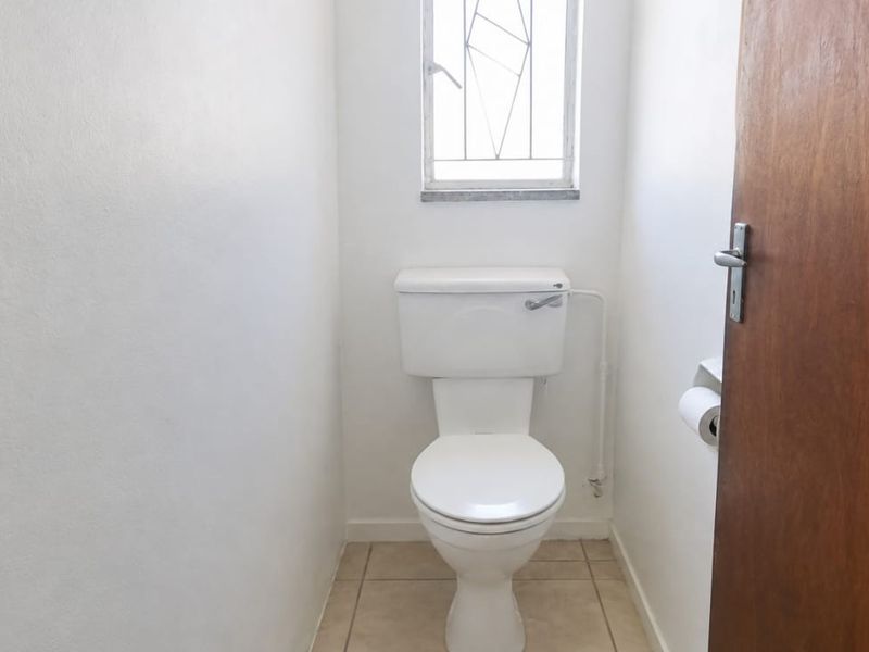 A compact, functional guest toilet featuring tiled flooring, a standard white toilet suite, and a window with security bars.