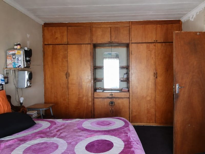 A bedroom featuring extensive built-in wooden cabinetry and a vanity mirror, requiring cosmetic updates to the wall finishes.