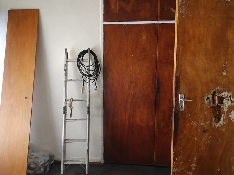 A vacant bedroom featuring built-in wooden cupboards and a damaged interior door requiring repair or replacement.