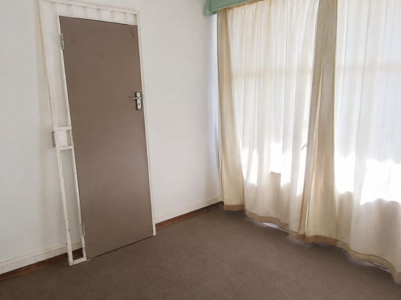 An empty bedroom featuring carpeted flooring, a security gate on the door, and large windows with curtain tracks.