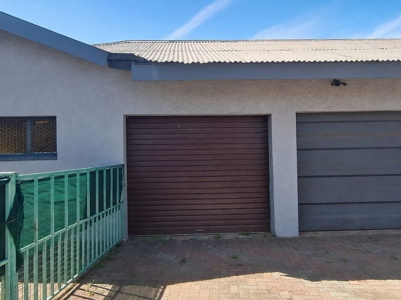 Exterior view of a double garage featuring mismatched doors, a corrugated metal roof, and a paved driveway area.
