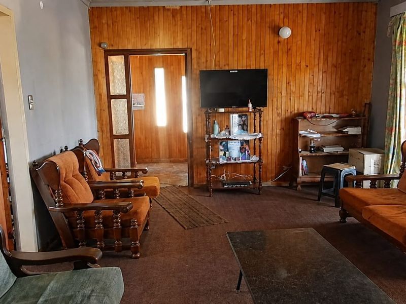 A living room featuring timber wall paneling, carpet flooring, and a glass panel door leading to an adjacent space.