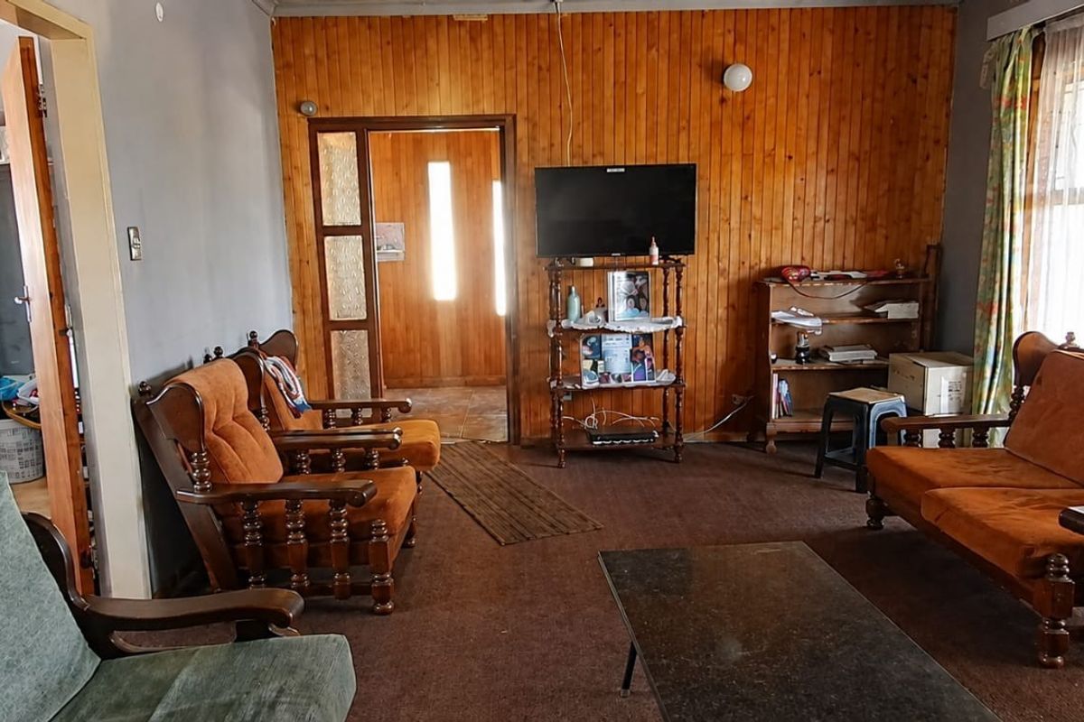A living room featuring timber wall paneling, carpet flooring, and a glass panel door leading to an adjacent space.