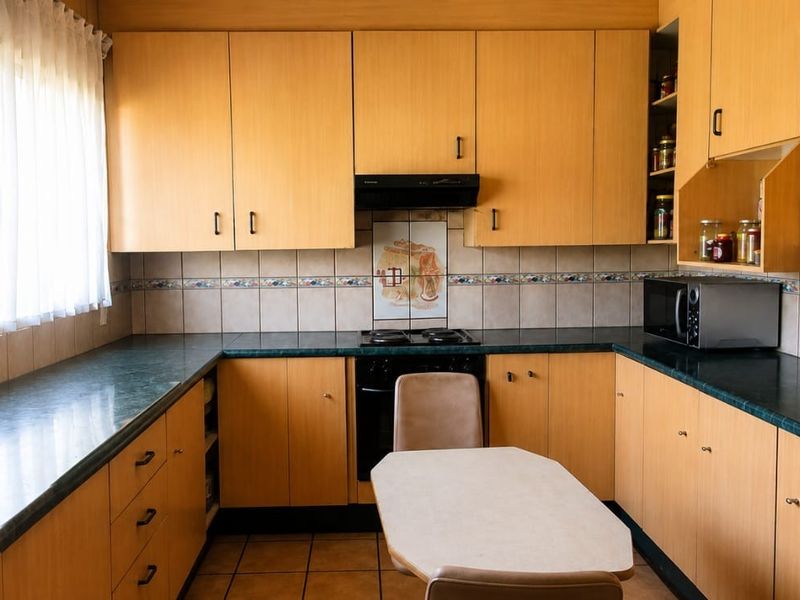 A functional kitchen featuring light wood-tone cabinetry, dark laminate countertops, a built-in oven with extractor fan, and tiled backsplash.