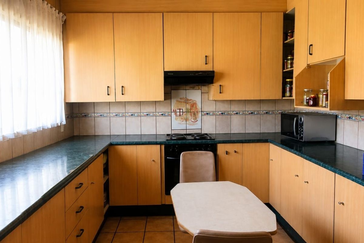 A functional kitchen featuring light wood-tone cabinetry, dark laminate countertops, a built-in oven with extractor fan, and tiled backsplash.