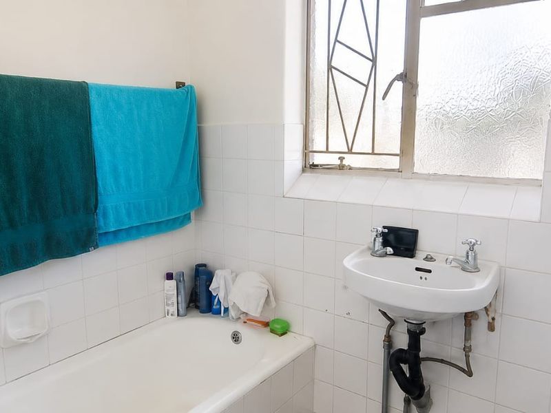A functional bathroom featuring a bathtub, wall-mounted basin, and tiled walls, with a window providing natural light and security bars.