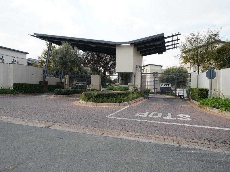 The secure entrance to the apartment complex features a modern gatehouse, paved driveway, and controlled access points for residents and visitors.