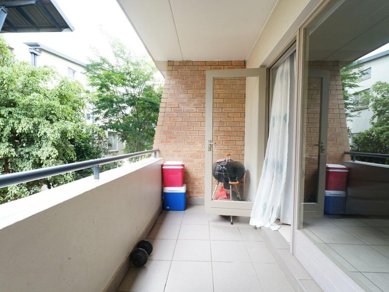 A covered balcony featuring tiled flooring, a brick feature wall, and a metal balustrade, providing an outdoor space accessible via sliding glass doors.