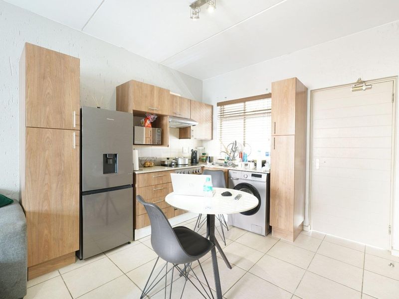 Compact open-plan kitchen featuring light wood-look cabinetry, tiled flooring, and integrated appliance space, creating a functional living and cooking area.