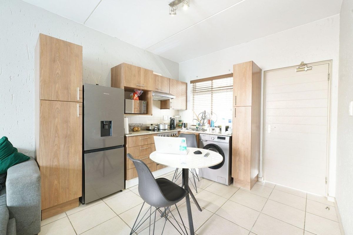 Compact open-plan kitchen featuring light wood-look cabinetry, tiled flooring, and integrated appliance space, creating a functional living and cooking area.