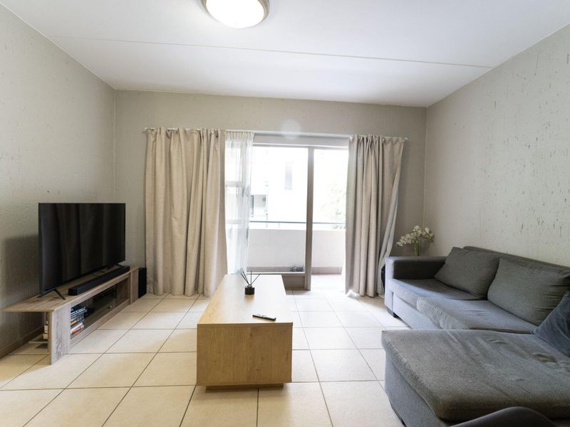 A living room featuring neutral tiled flooring and a sliding glass door providing access to an outdoor balcony area.