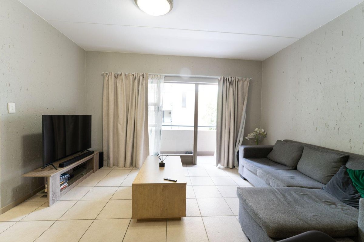 A living room featuring neutral tiled flooring and a sliding glass door providing access to an outdoor balcony area.