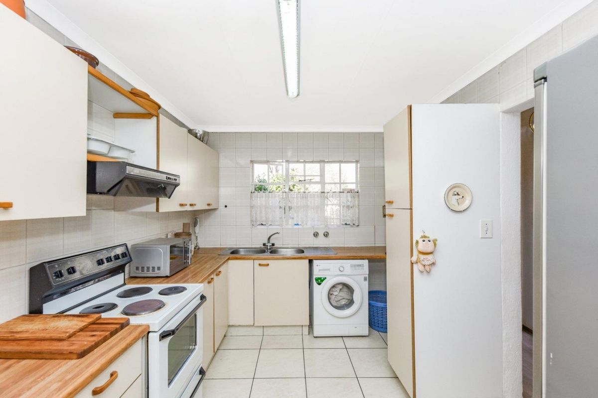 A functional kitchen featuring tiled flooring, laminate countertops, built-in cabinetry, and a double basin sink with a tiled backsplash.
