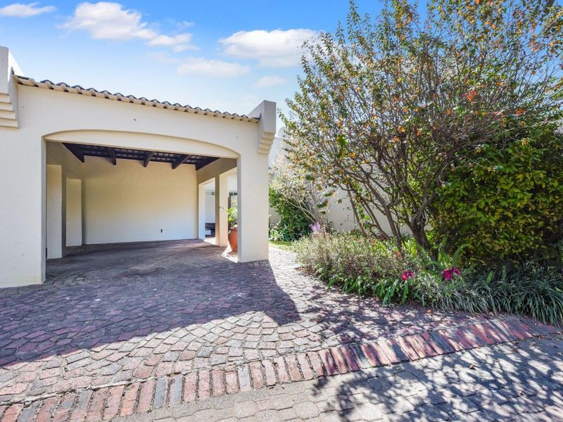 A well-maintained front exterior featuring a covered carport, cobblestone driveway, and established garden landscaping.