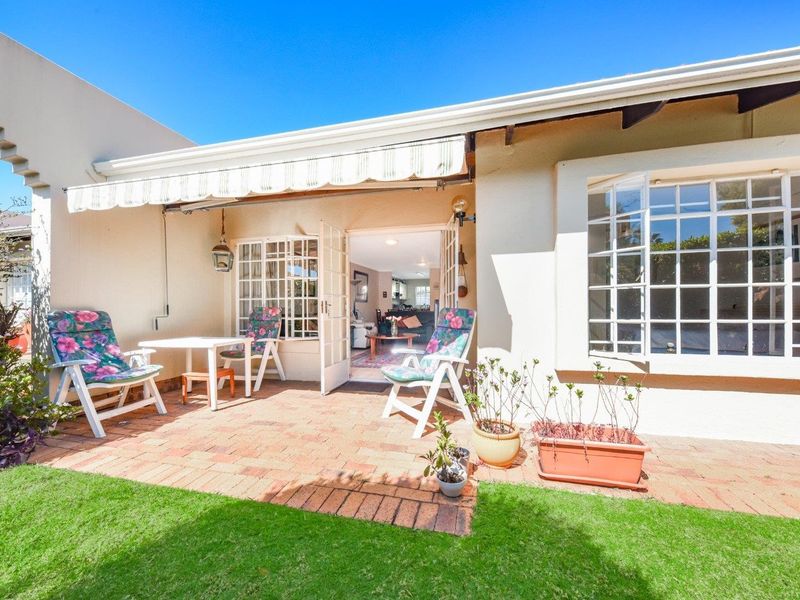 A sunny paved patio area featuring a retractable awning, classic french doors, and a bay window, providing seamless access to the interior living space.