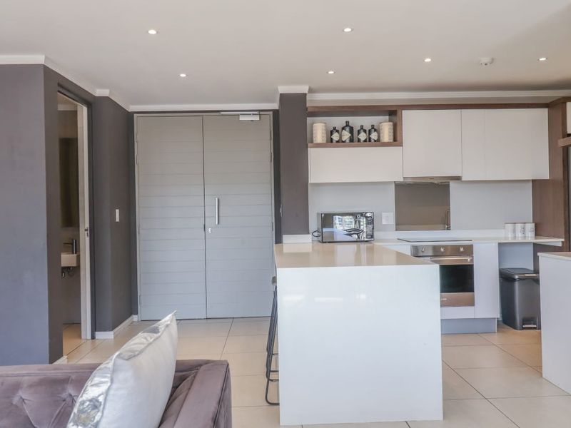 Modern open-plan kitchen featuring a central island, sleek white cabinetry, integrated appliances, and recessed lighting, seamlessly connected to the living area.