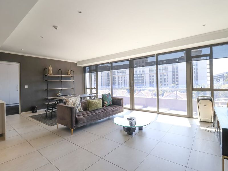 Spacious open-plan living area featuring large sliding glass doors that open to a balcony, providing ample natural light and modern tiled flooring.