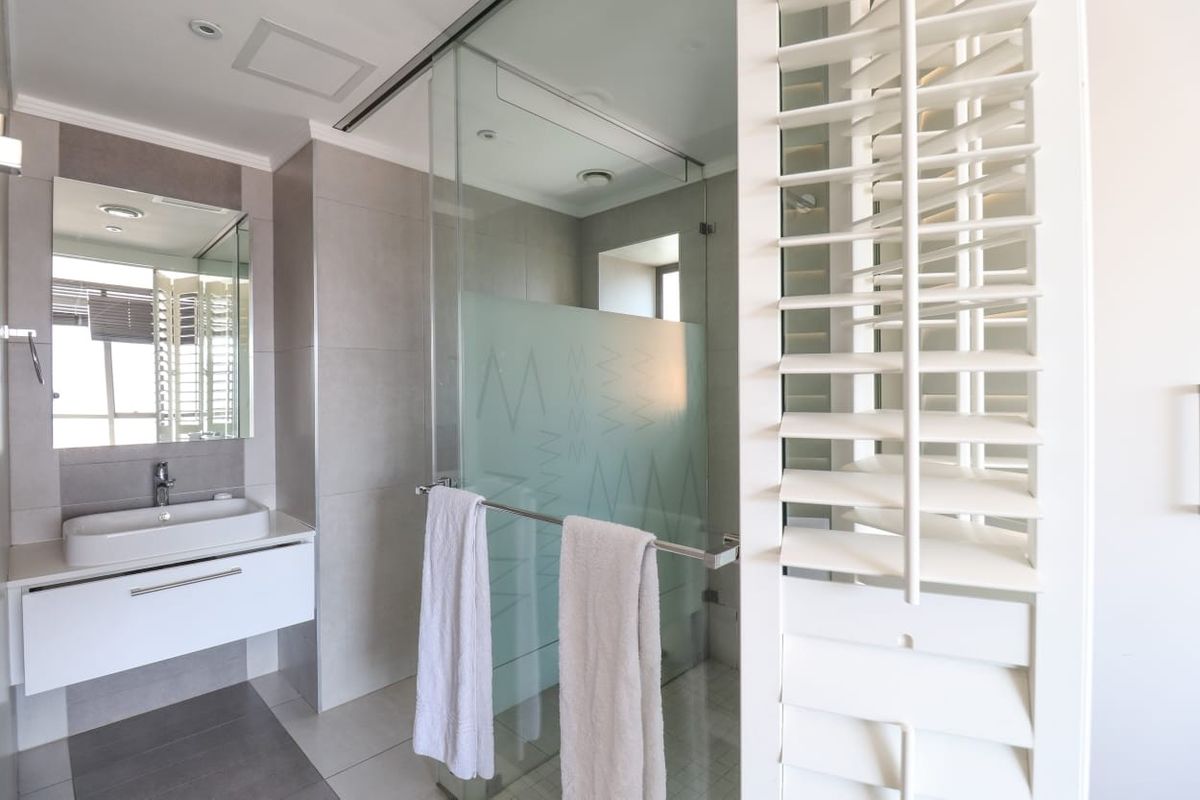 Modern bathroom featuring a wall-mounted vanity with vessel sink, glass-enclosed shower, and white plantation shutters for natural light control.