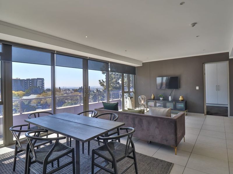 Spacious open-plan living and dining area featuring large sliding glass doors that open to a balcony with expansive city views.